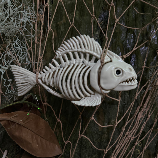 Plastic fish skeleton hanging from some fishing net with foliage around